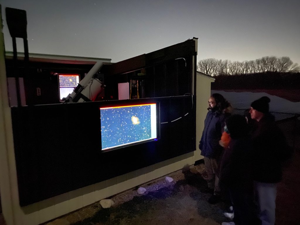 Visitors outside the DVO at night watching a live image of a galaxy on the screen in its south wall