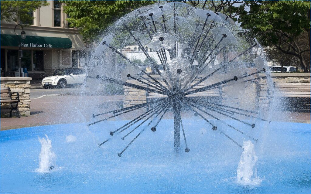 The Dandelion Fountain on the Naperville Riverwalk, a sphere of water jets, with Egg Harbor Cafe across the street.