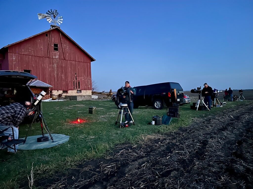 Members setting up telescopes beside a red barn at dusk for a dark-sky observing night