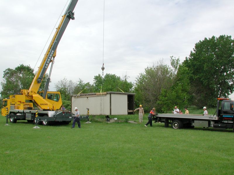 A crane and a flatbed truck beside the old Riley Observatory building, with club members watching