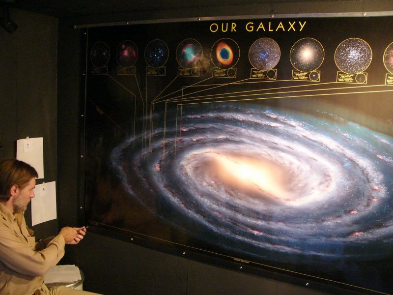 A member presenting at the Our Galaxy exhibit, a wall-sized illustration of the Milky Way