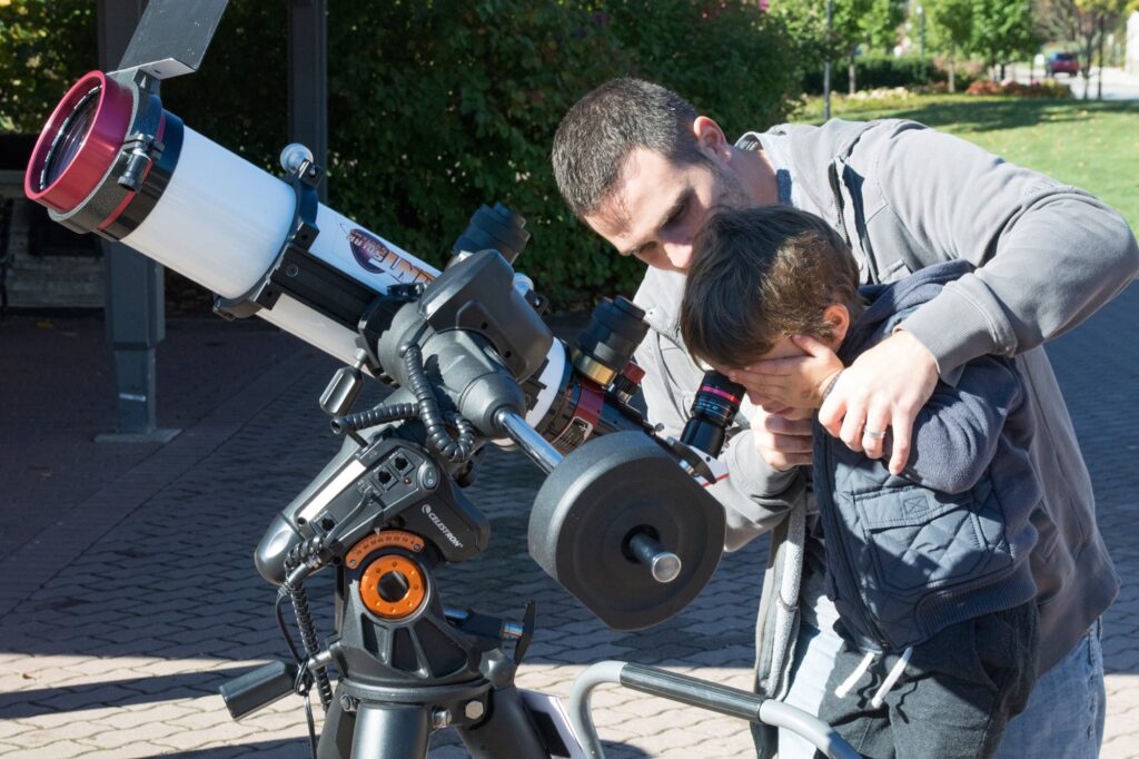 A member helping a child look through a solar telescope on the Riverwalk